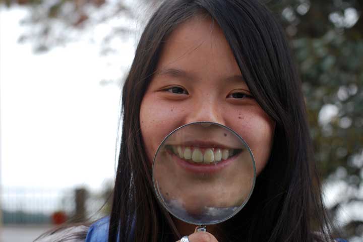 A student similes through a magnifying glass